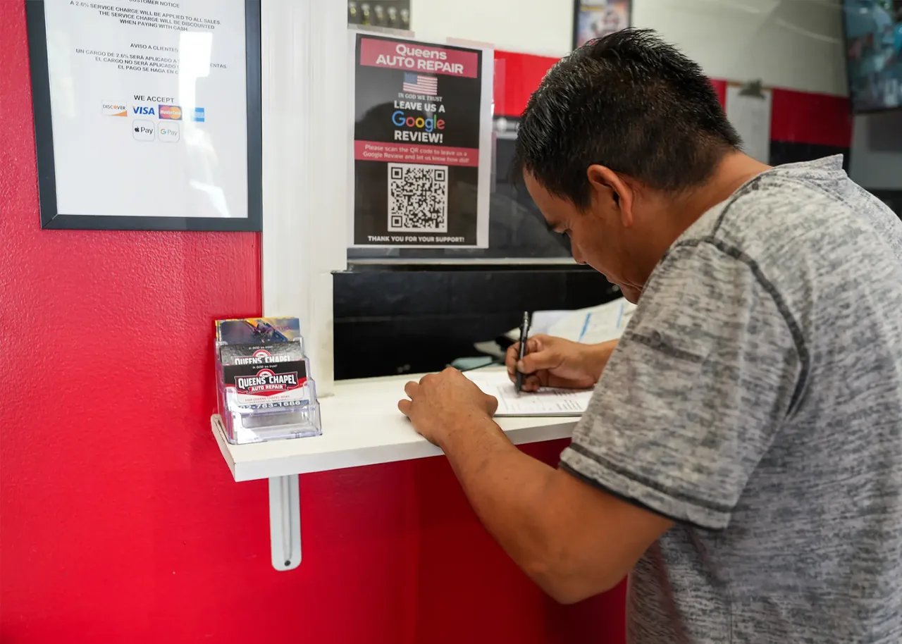 Customer at the Queens Auto Repair front desk with the shop's Google Review sign visible